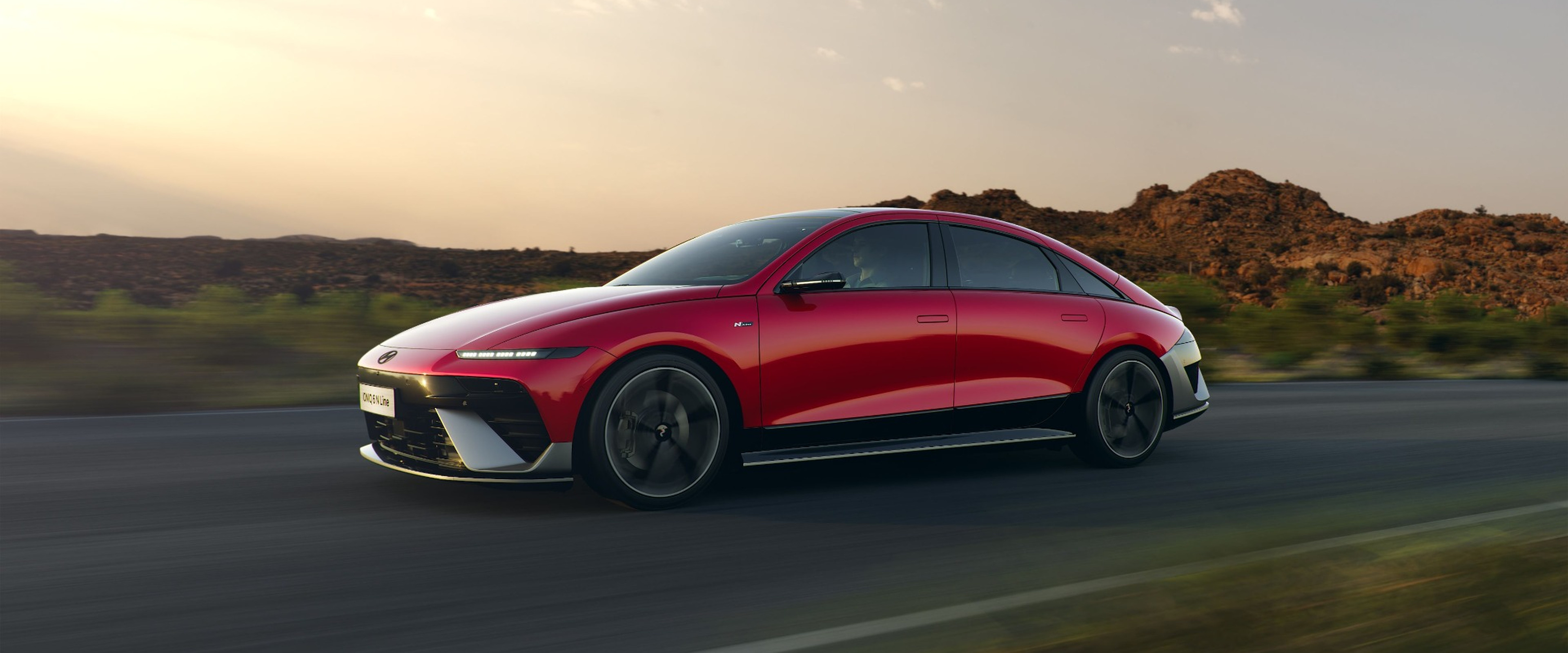 Red Hyundai IONIQ 6 driving along an open road at sunset